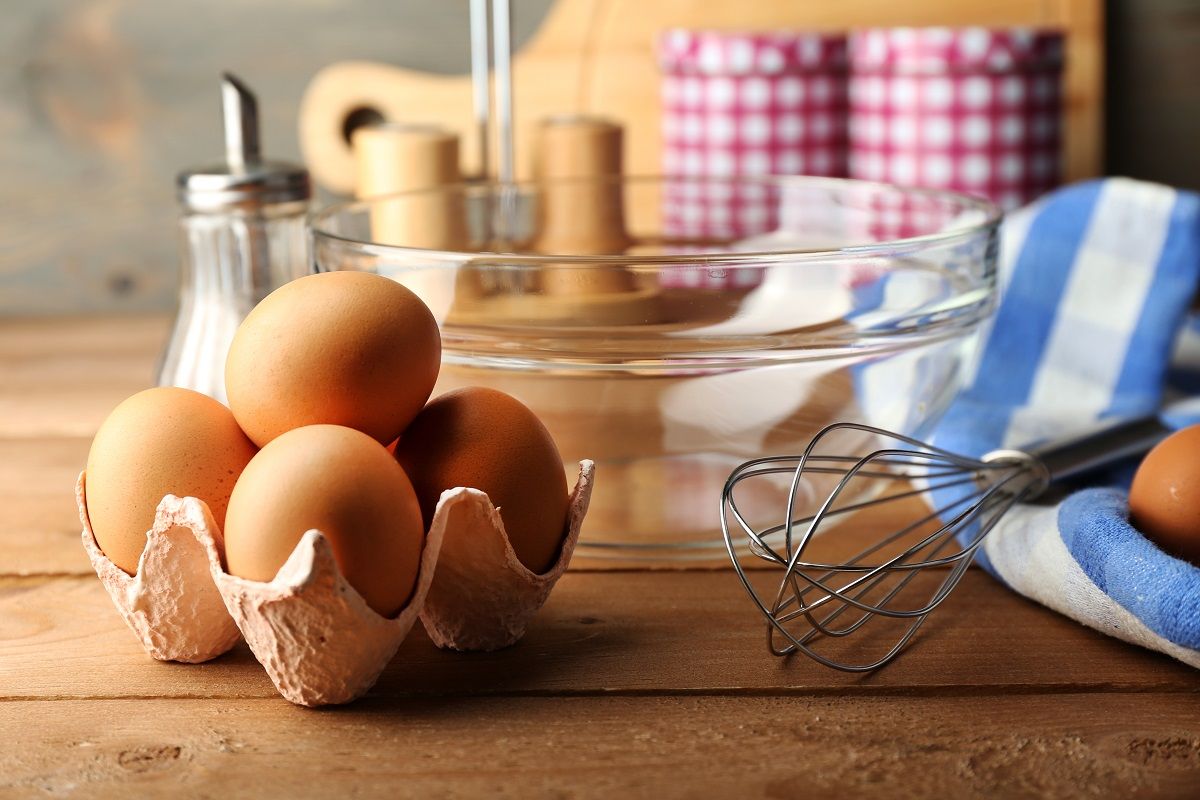 Preparation cream with eggs in glass bowl on wooden background