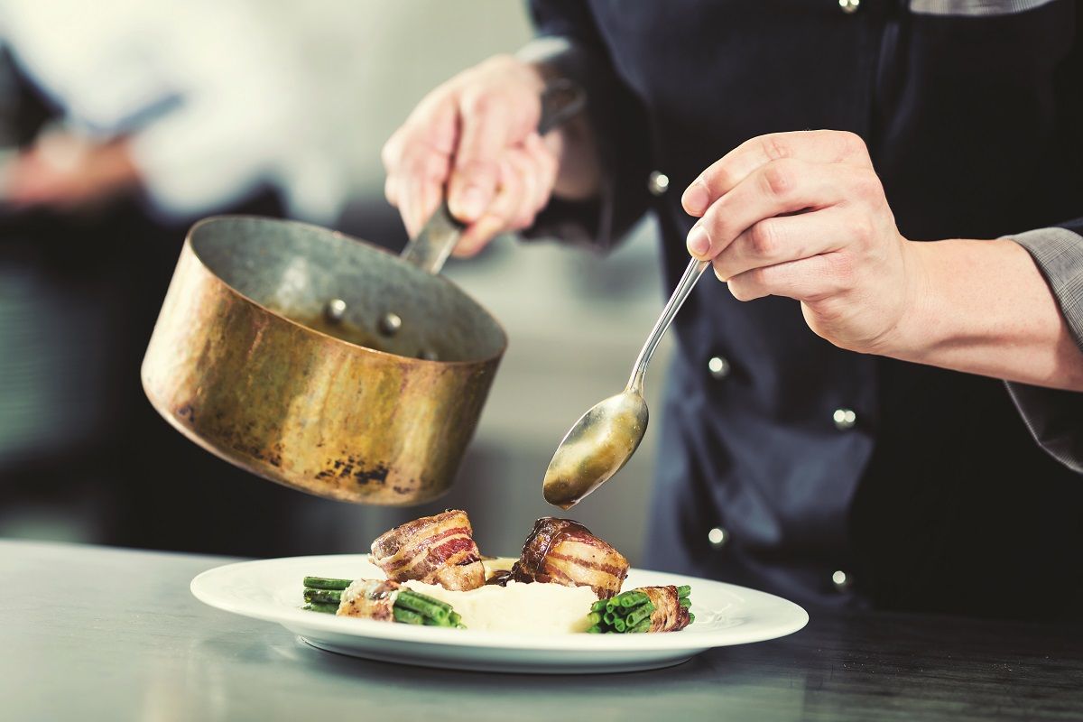 Chef pouring sauce on dish in restaurant kitchen