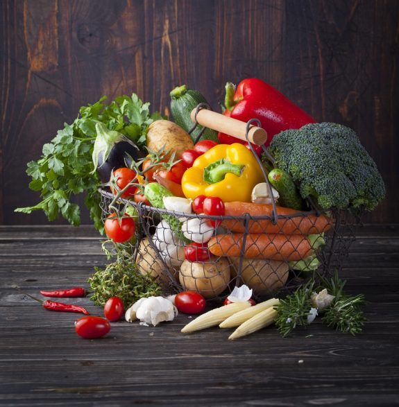 Vegetables variety in a wire basket on wooden background.