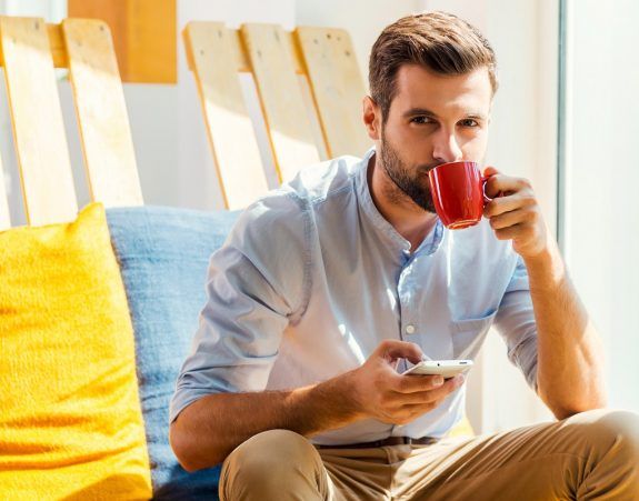 Inspired with cup of fresh coffee. Handsome young man holding mo