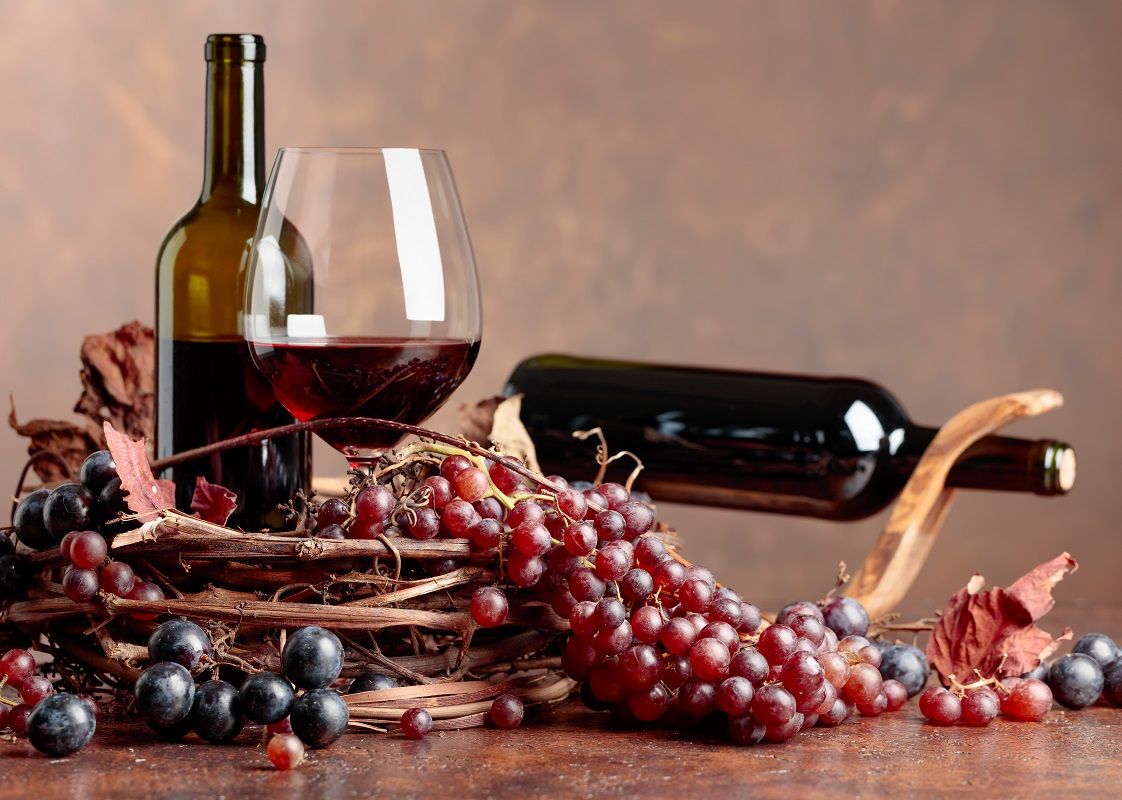 Red wine and fresh grapes with dried up vine leaves.
