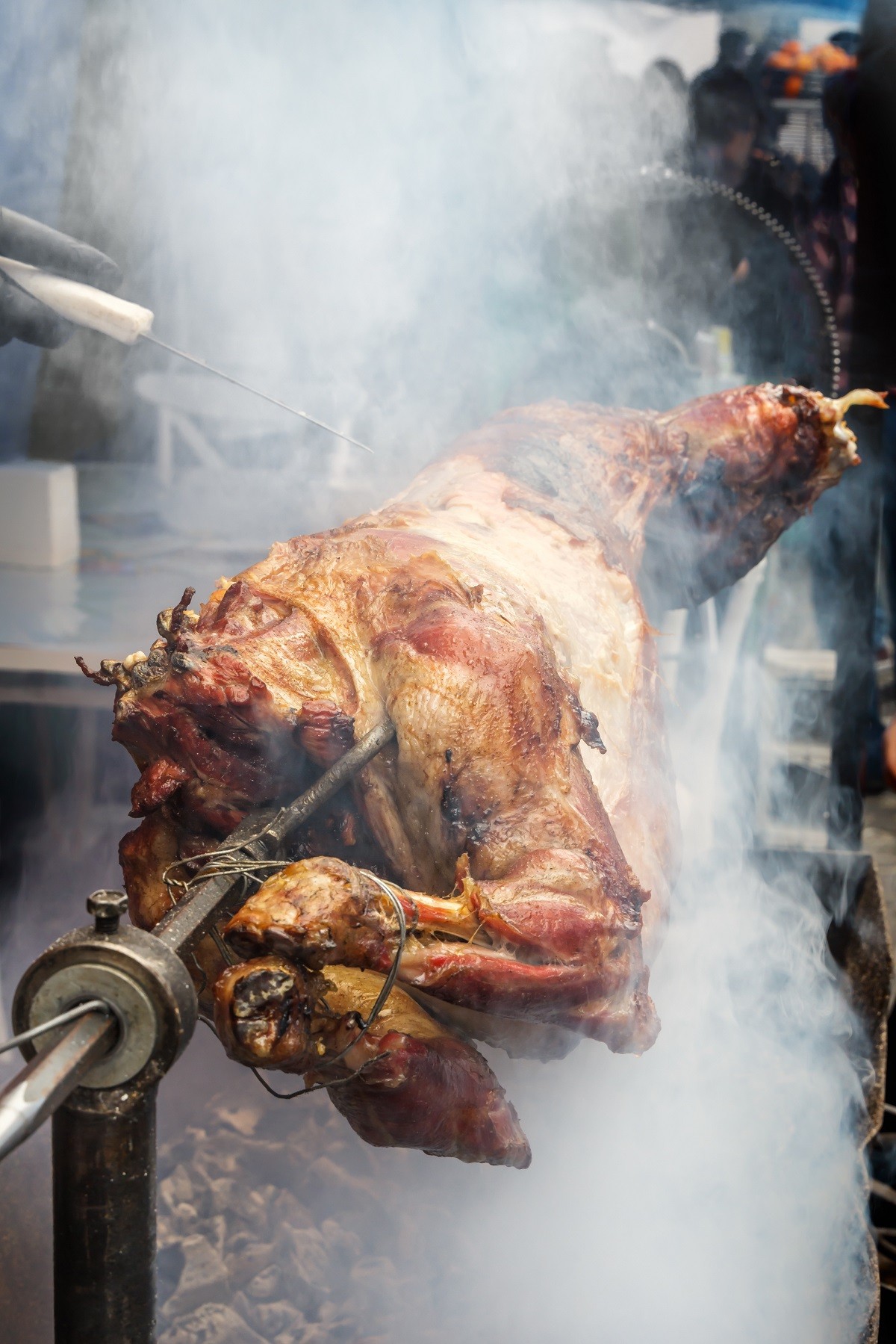 Cook’s hand with a knife checks the readiness of the lamb on a s