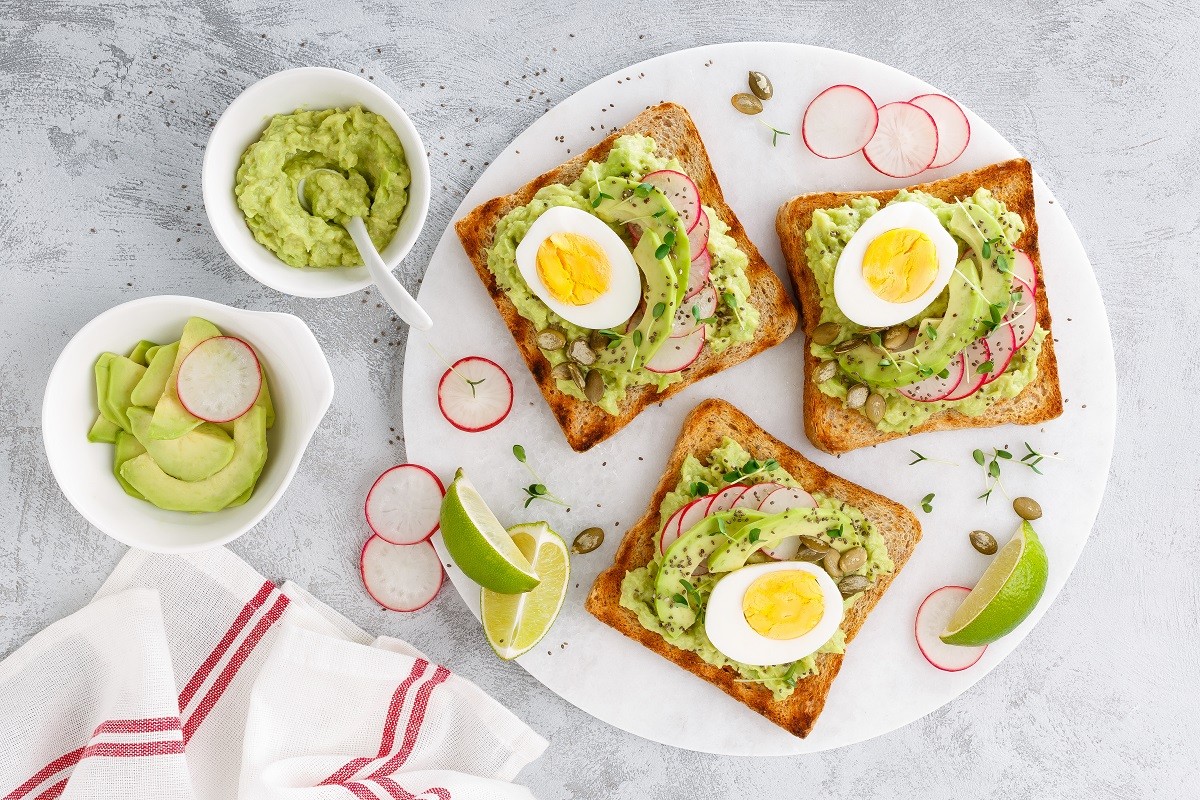 Toasts with avocado guacamole, fresh radish, boiled egg, chia and pumpkin seeds. Diet breakfast. Delicious and healthy plant-based food. Flat lay. Top view