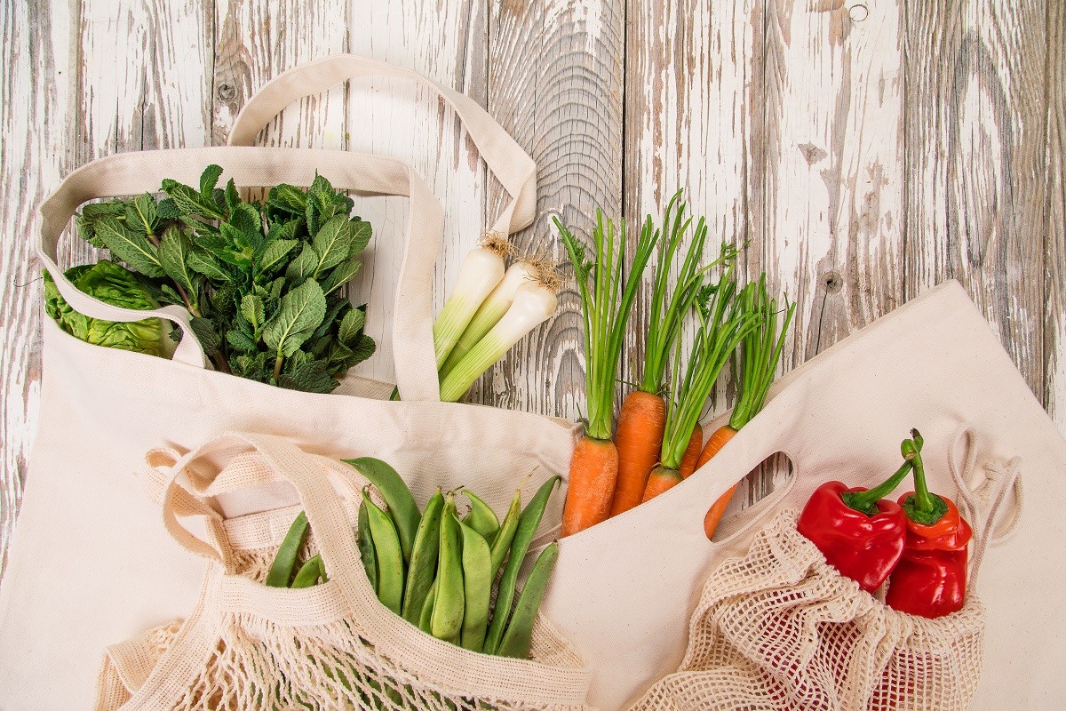 Fresh vegetables in bio eco cotton bags on old wooden table. Zero waste shopping concept.