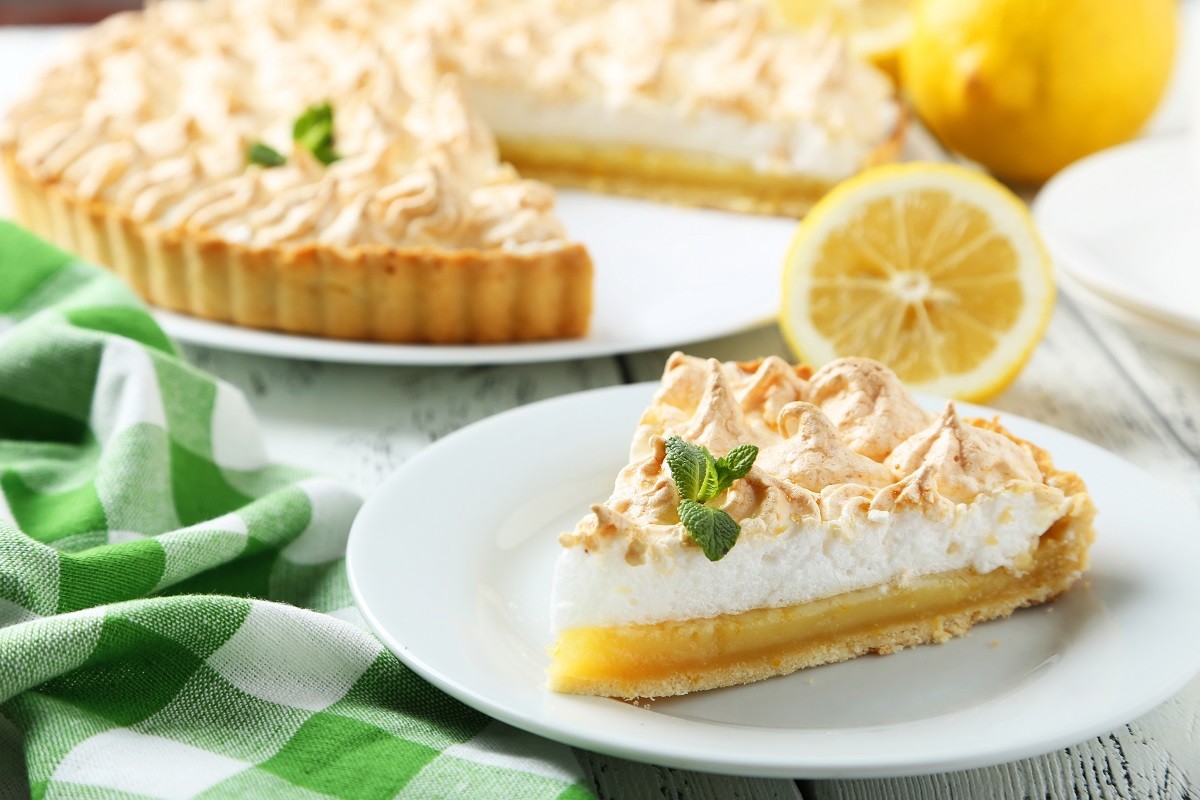 Lemon meringue pie on plate on white wooden background