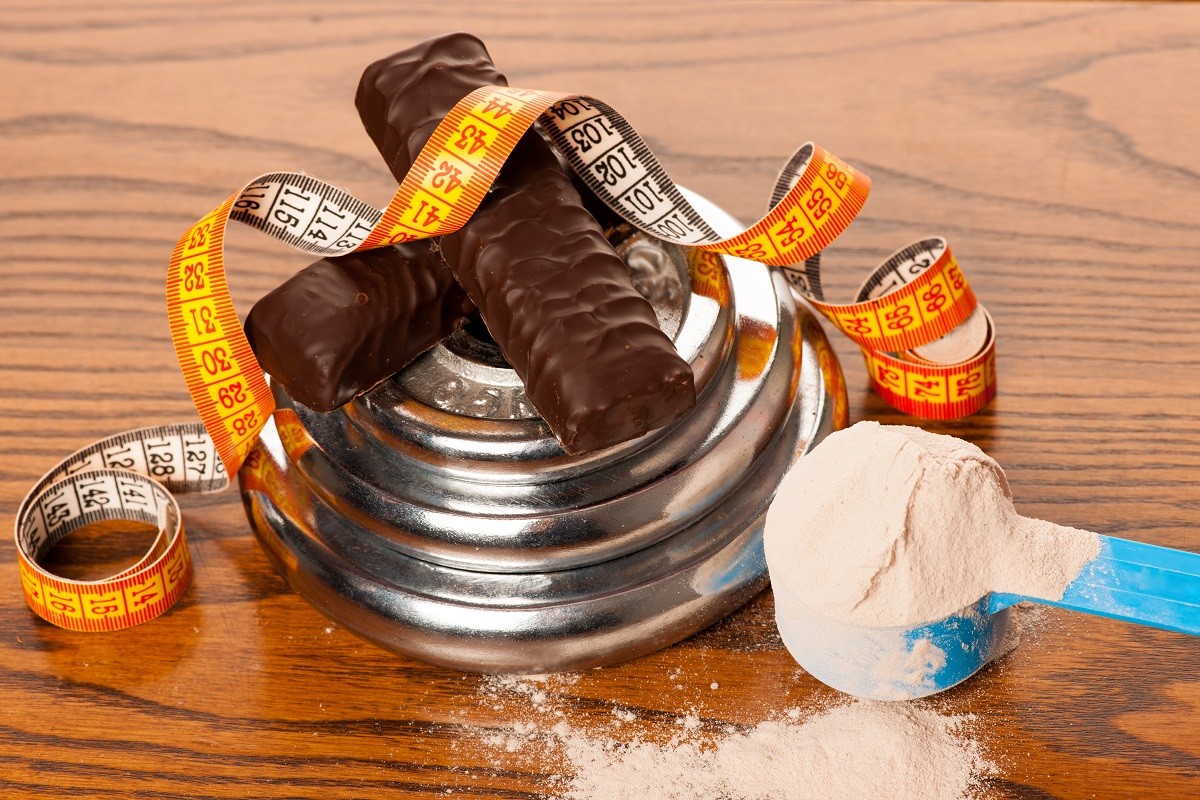 Whey protein powder in measuring scoop, protein bar, meter tape