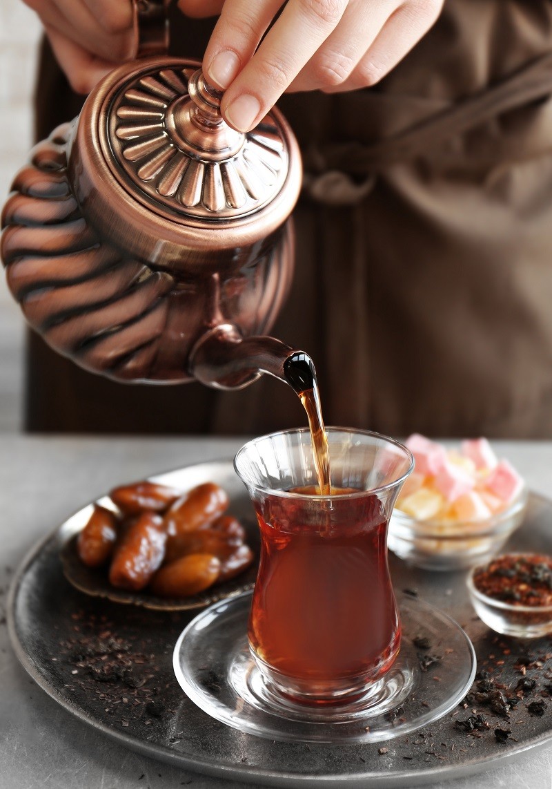 Female hands pouring Turkish tea into traditional glass on metal tray closeup