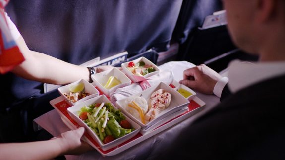 Midsection of stewardess holding tray with airplane food on blue background. Stewardess brought lunch, businessman, first class, high level of service on the plane