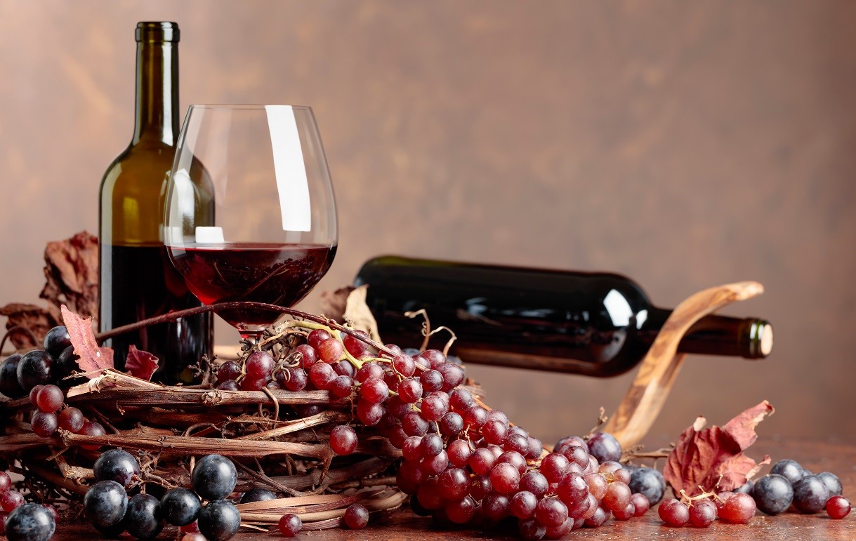 Red wine and fresh grapes with dried up vine leaves.