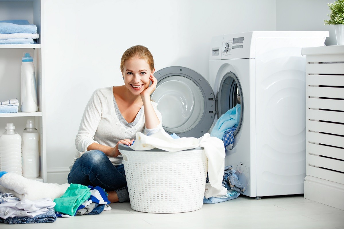happy woman housewife in the laundry room near the washing machine with dirty clothes