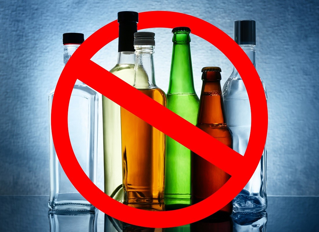 Different alcohol drinks in bottles with STOP sign on grey background