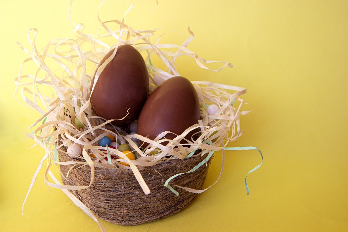 Wicker basket with chocolate easter eggs and candy on yellow background