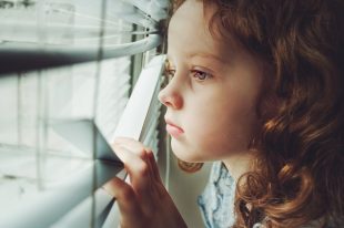 Little child looking out the window through the blinds. Backgrou