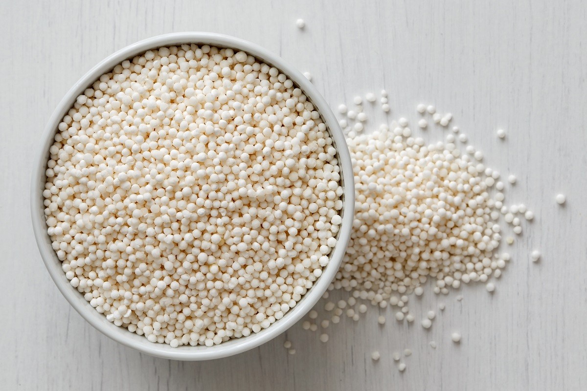 Dry tapioca pearls in white ceramic bowl isolated on painted white wood from above. Spilled tapioca.