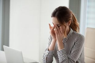 Tired young woman massaging nose bridge at workplace