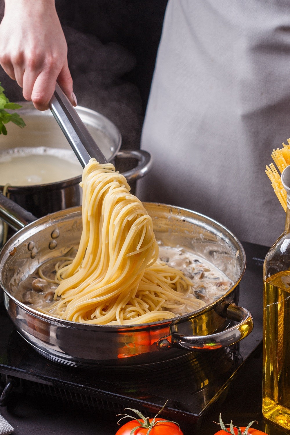 young woman in a gray apron preparing pasta