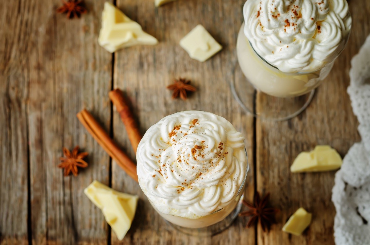 Hot white chocolate with whipped cream and cinnamon on a wood ba