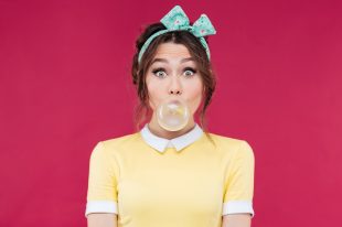 Amazed cute pinup girl blowing a bubble gum balloon