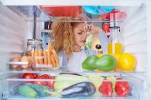 Womann standing in front of opened fridge and holding up to her