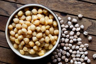 Cooked chickpeas in brown ceramic bowl on dark from above. Spilled dry chickpeas.