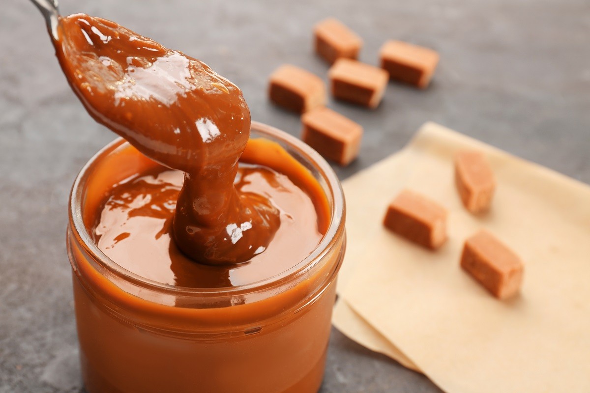 Glass jar with tasty caramel sauce and spoon on table
