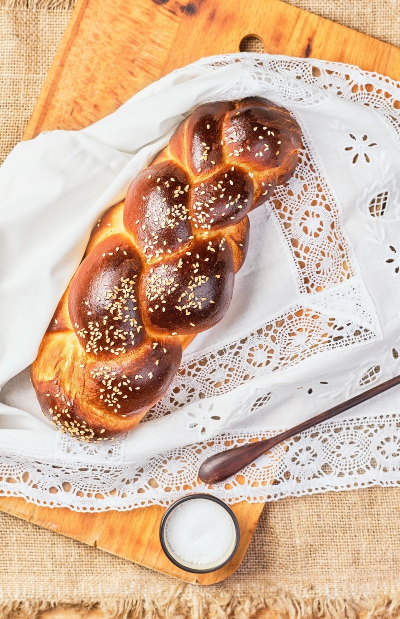 Fresh homemade challah with sesame seeds on a white lace napkin. Top view, challah for Saturday