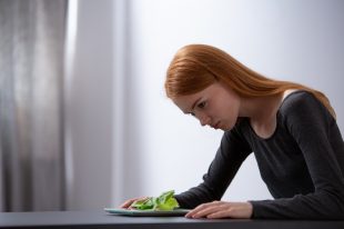 Redhead teenage girl on diet sitting at table and looking at plate with lettuce