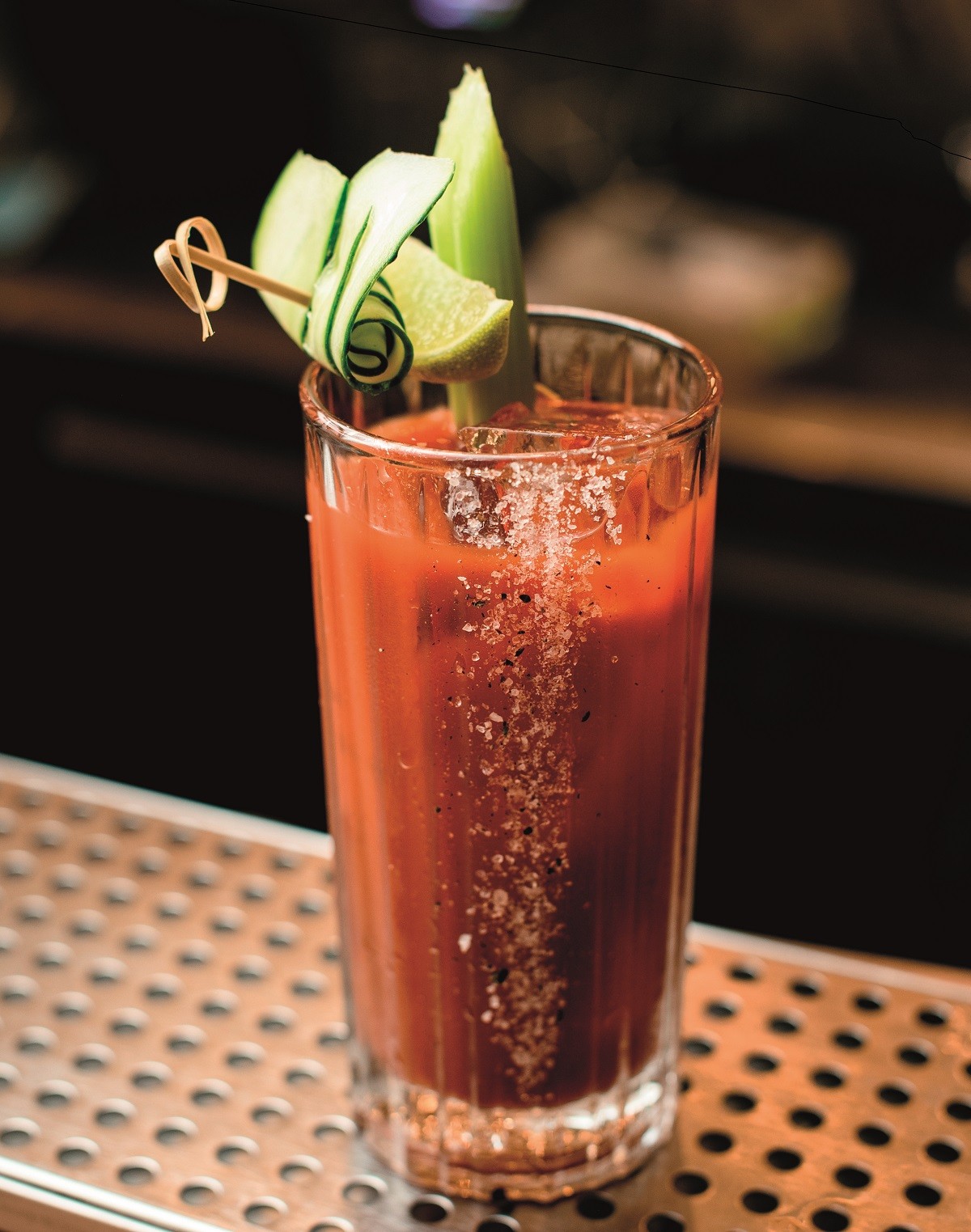 view on glass of cocktail garnished with slices of fresh vegetables stands on the bar counter