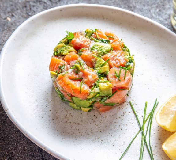 PERUVIAN FOOD. Salmon ceviche with avocado, spring onion and lemon on white plate served with white wine