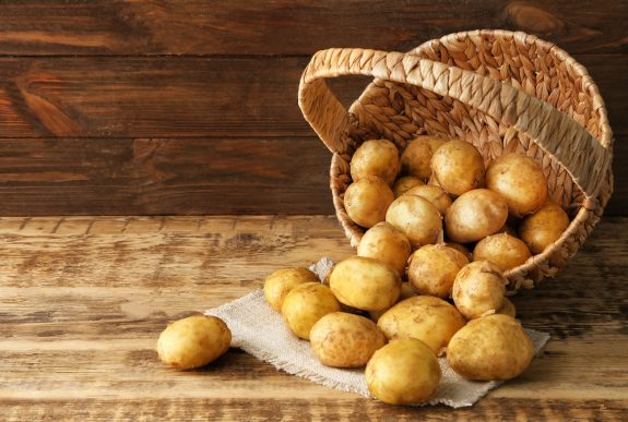 Wicker basket and young potatoes on wooden table