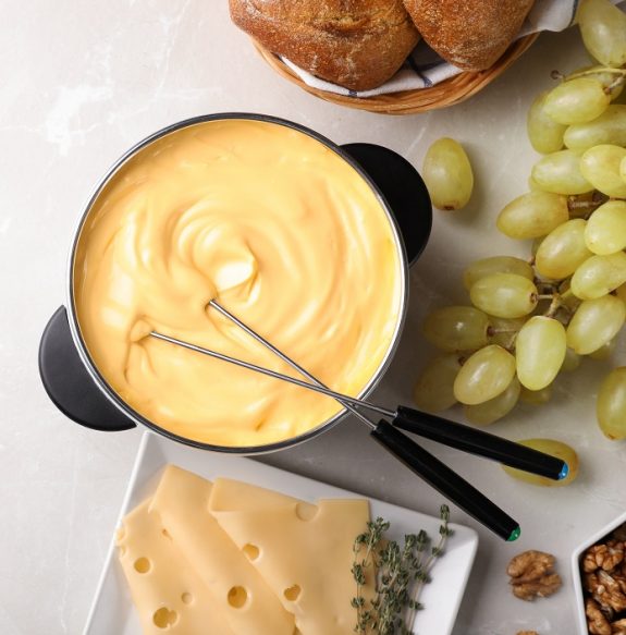 Flat lay composition with pot of delicious cheese fondue and space for text on gray table