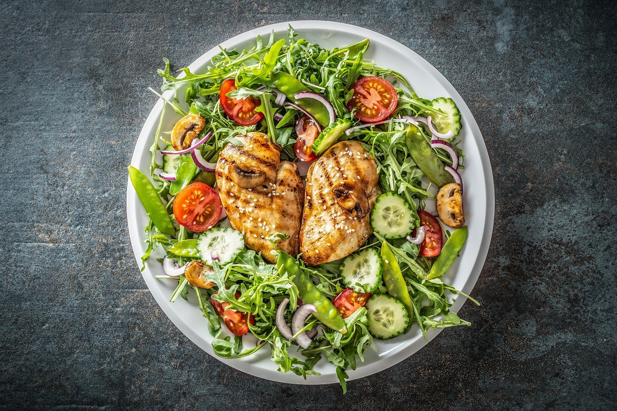 Top view of a healthy chicken salad in a white plate placed on the black rustic surface.