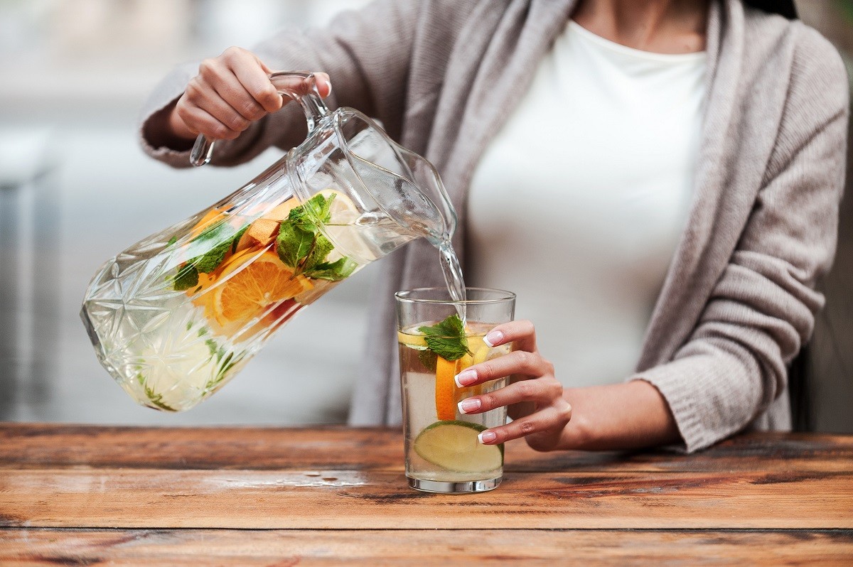Healthy drink for healthy life. Close-up of young woman pouring fresh lemonade to glass while standing at the wooden desk