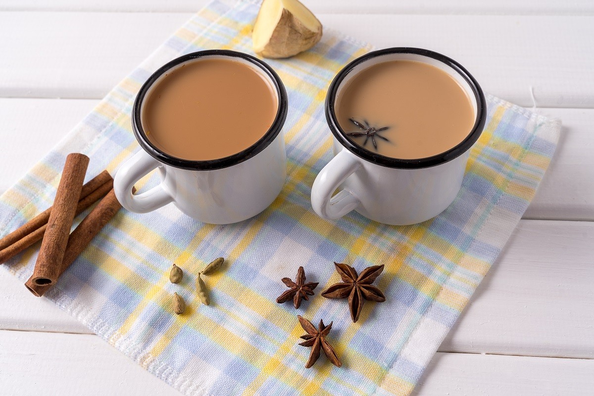 Masala chai tea in a mugs and kitchen herbs, over white table background.