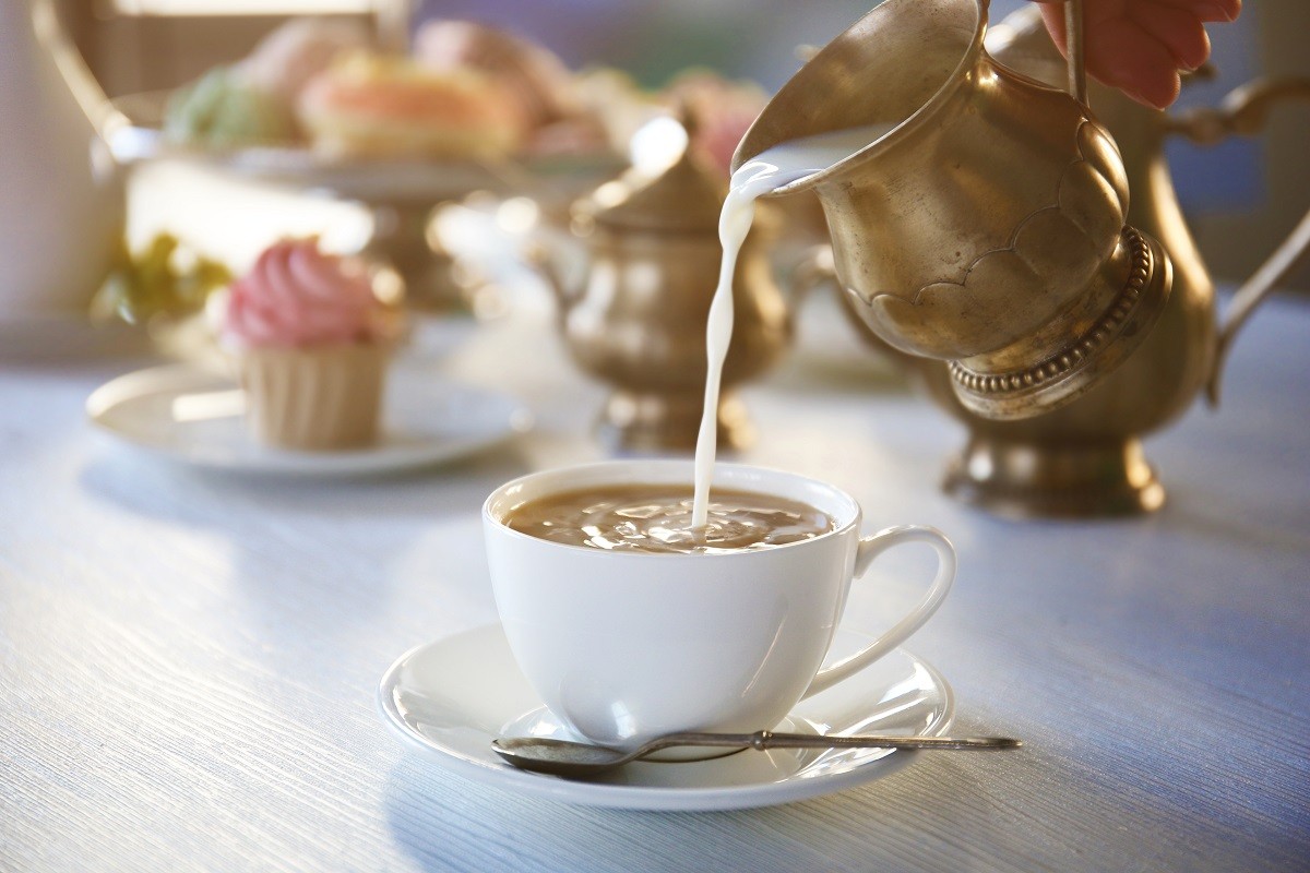 Pouring milk into cup of tea on wooden table closeup