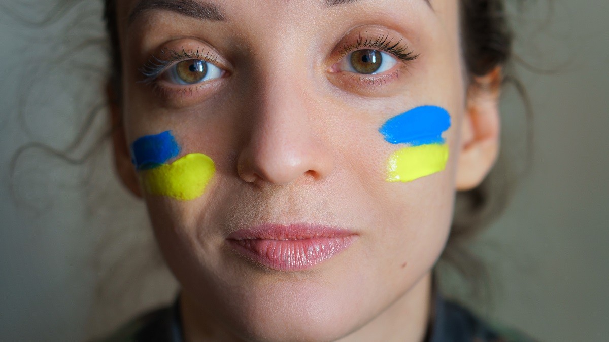 Indoor portrait of young girl with blue and yellow ukrainian flag on her cheek wearing military uniform, mandatory conscription in Ukraine, equality concepts