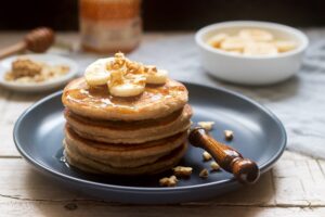 Pancakes with banana, nuts and honey, served with tea. Rustic style.