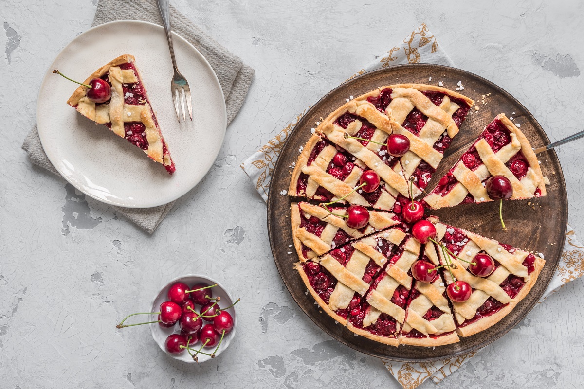 One piece on a plate and the whole homemade cherry pie on white background, top view