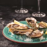 Opened fresh oysters on a blue plate, served with lemon and ice.