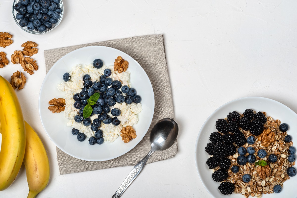 Healthy breakfast. Cottage cheese with blueberry, nuts, honey and mint in a white bowl on a white background. Top view. Copy Space.