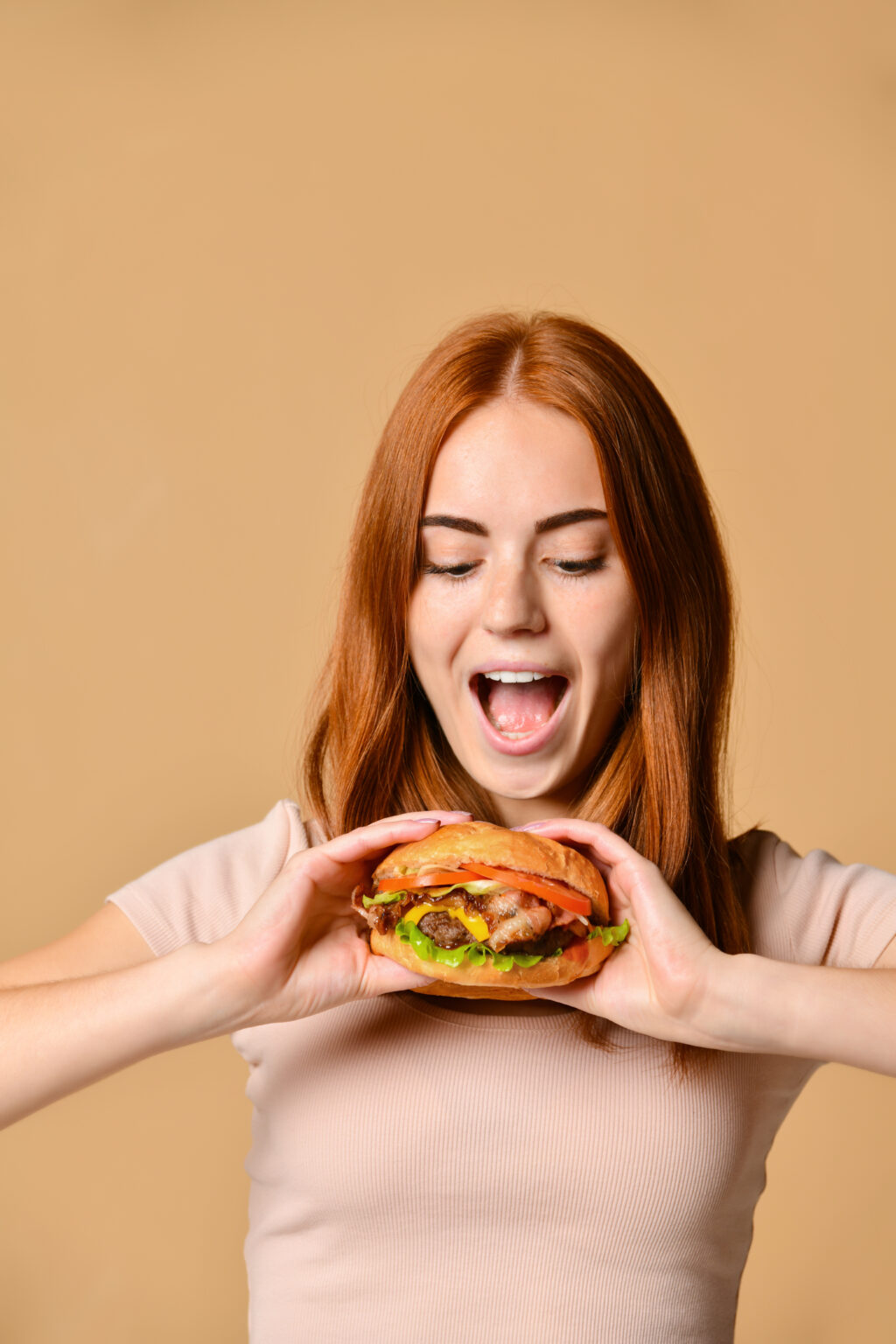Close up portrait of a hungry young woman eating burger isolated over nude background