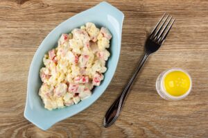 Blue plate with crab sticks salad, fork, salt shaker on table. T