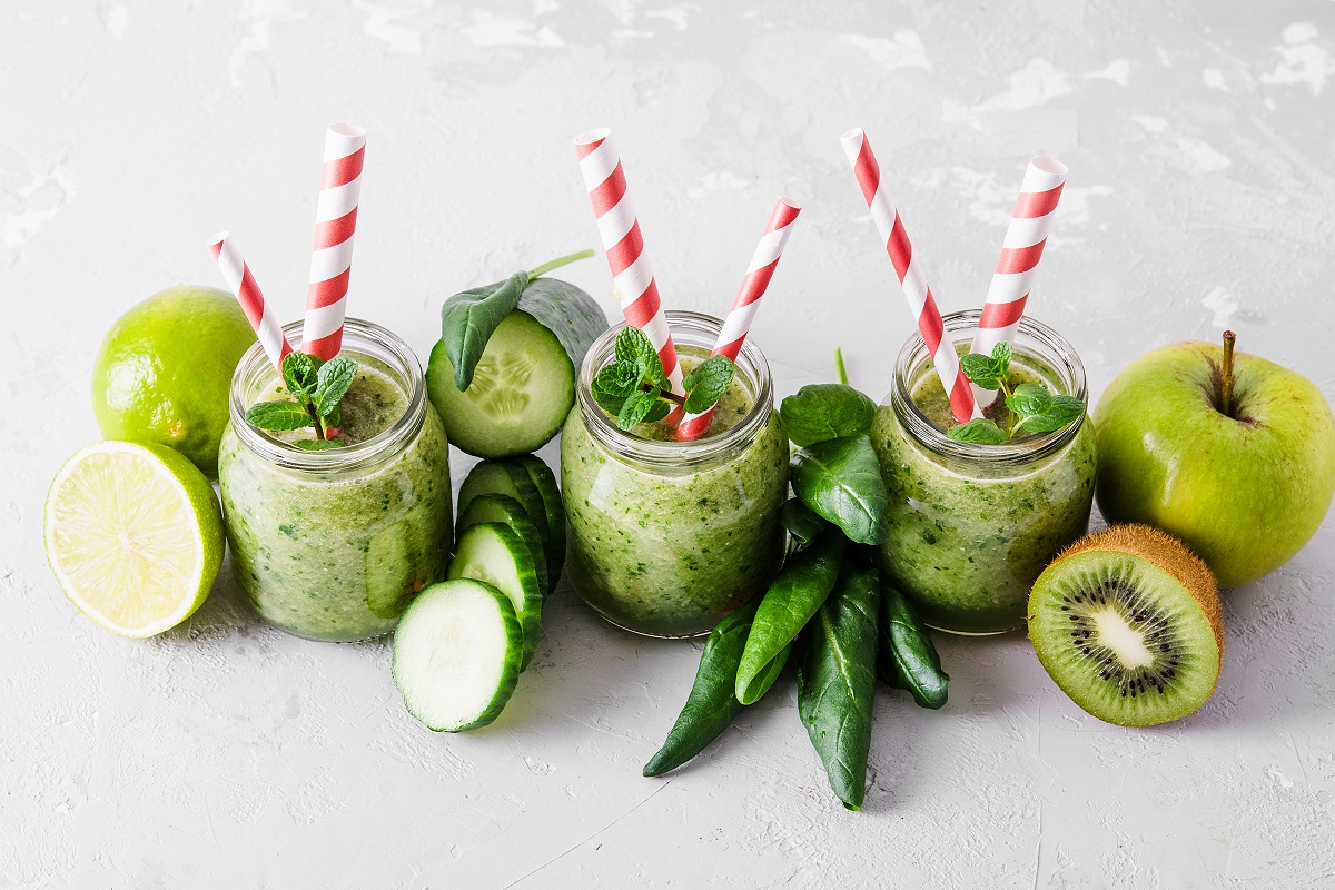 Jars with green smoothie and red tubules on a light background. Freshly made vegetable smoothie. Close-up. Glass jars with green smoothies in a row.