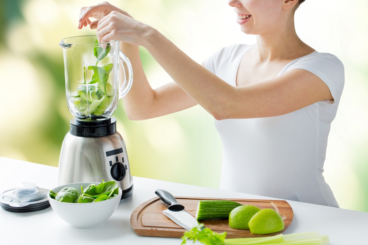 close up of woman with blender and vegetables