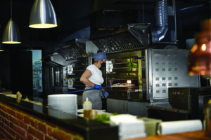 Restaurant professional open kitchen, Woman in a mask on her face, preparing pizza, new measures to fight the virus