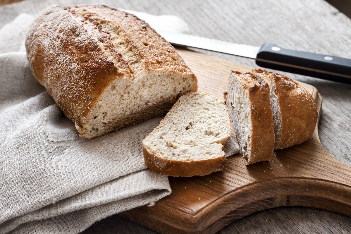 Loaf of whole wheat bread with slices on wooden board
