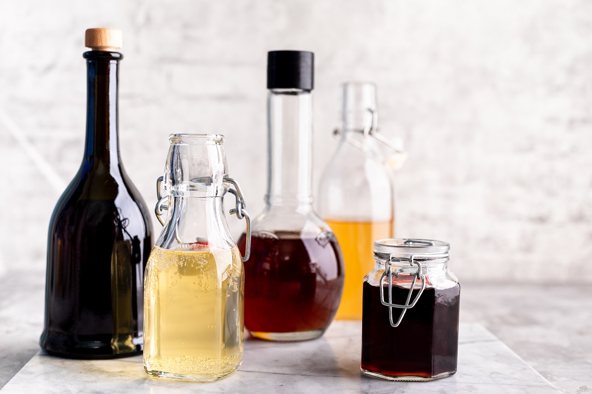 Original glass bottles with different vinegar on a marble table against a background of a white brick wall. Copy space.