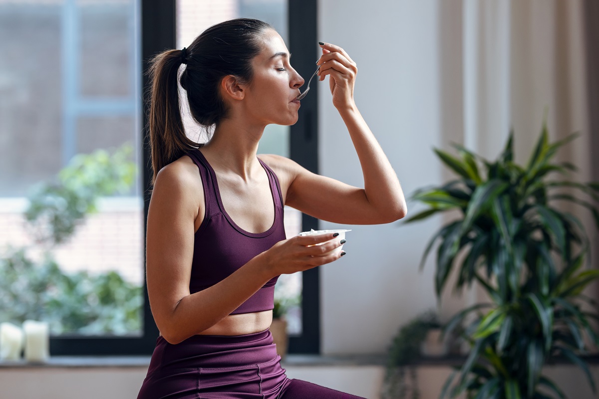 Shot,Of,Sporty,Young,Woman,Eating,A,Yogurt,While,Sitting