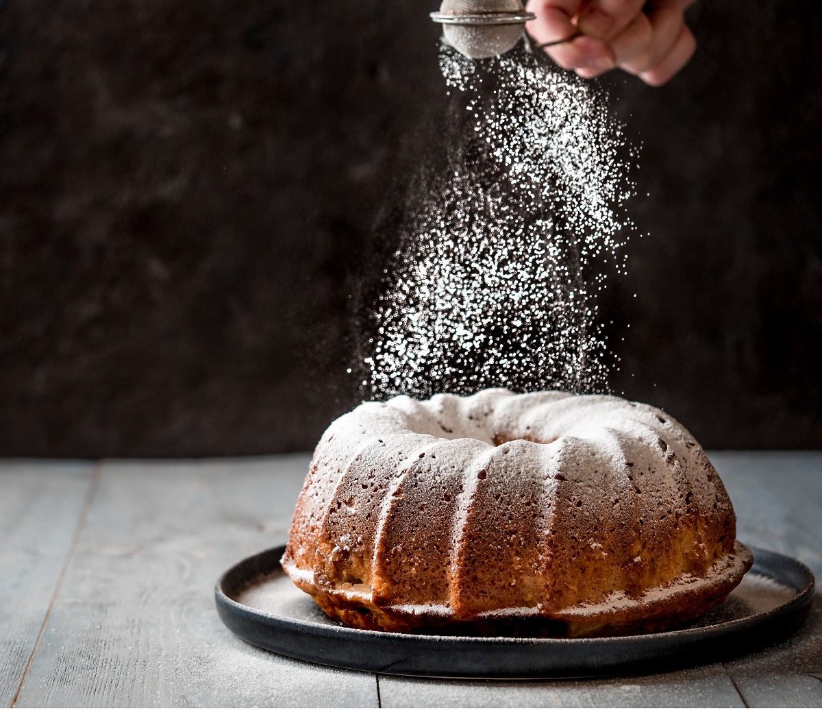 Woman’s,Hand,Sprinkling,Icing,Sugar,Over,Fresh,Bundt,Cake.,Powder