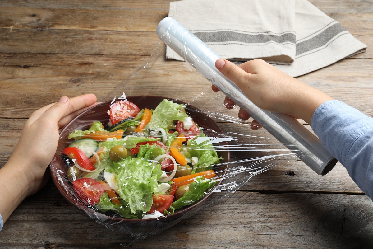Woman,Putting,Plastic,Food,Wrap,Over,Bowl,Of,Fresh,Salad